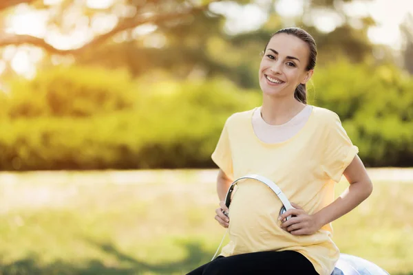 穿着黄色 t恤衫的孕妇坐在瑜伽球上, 听音乐 — 图库照片