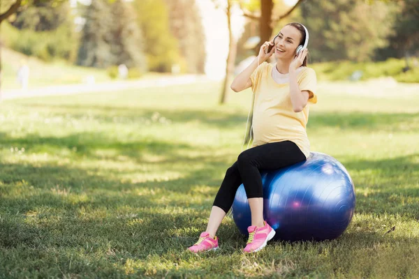 Schwangere im gelben T-Shirt sitzt auf einem Yoga-Ball und hört Musik — Stockfoto