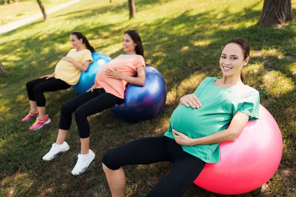 Três mulheres grávidas deitam-se em bolas de ioga no parque. Eles seguram suas barrigas — Fotografia de Stock