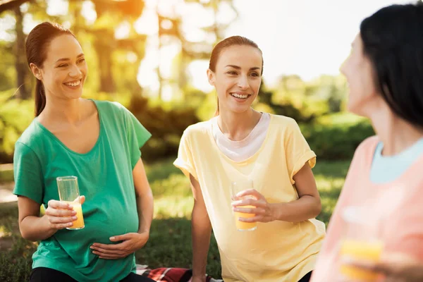 Tre gravida kvinnor sitter i parken efter öva yoga och dricker juice. De vilar — Stockfoto