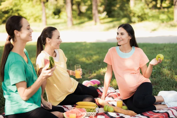 Üç hamile kadın Parkta piknik için bir halı üzerinde oturup yemek. Tüm gülümsüyor musun — Stok fotoğraf