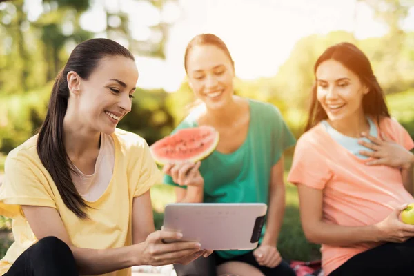 Drie zwangere vrouwen rusten op natuur na het doen van yoga. Één van hen heeft een tablet — Stockfoto