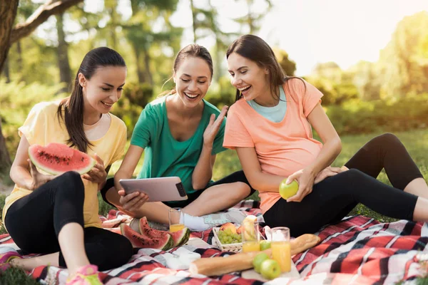 Trois femmes enceintes reposent sur la nature après avoir fait du yoga. L'un d'eux tient une tablette. — Photo