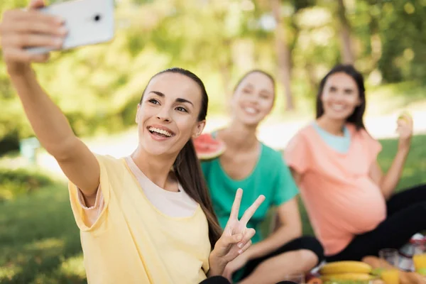 A pregnant woman in a yellow T-shirt sits with her pregnant girlfriends on a picnic in the park and makes a selfie — Stock Photo, Image
