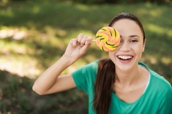 Pregnant woman in green T-shirt posing in park with colored candy — Stock Photo, Image