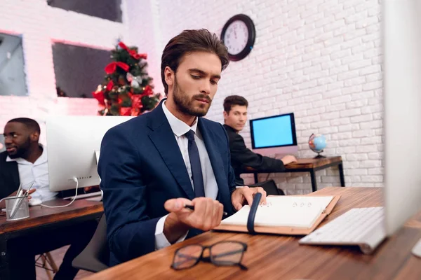 People work on the eve of the new year. In the foreground is a man who sits at his workplace and works.