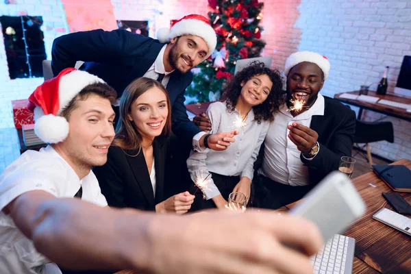 People are preparing to meet the new year in the office. They sit with champagne glasses in their hands and make selfies