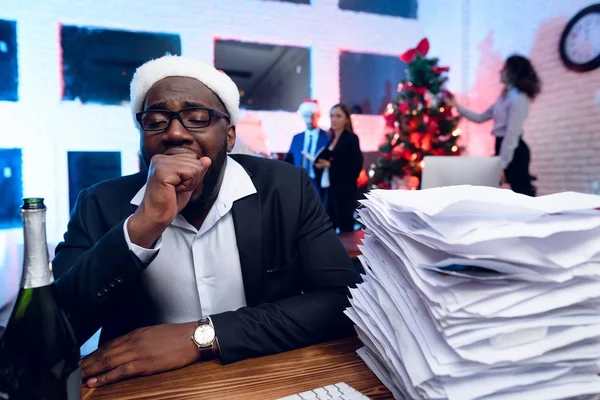 Un hombre negro está sentado en su escritorio en Nochevieja. Tiene mucho trabajo y está muy cansado. . — Foto de Stock