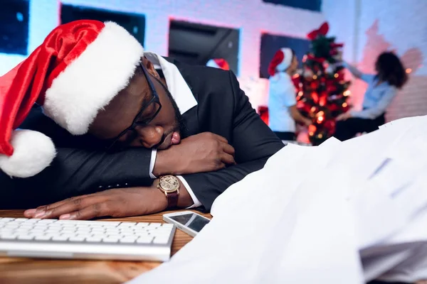 A black man is sitting at his desk on New Year\'s Eve. He has a lot of work and he fell asleep at the table.