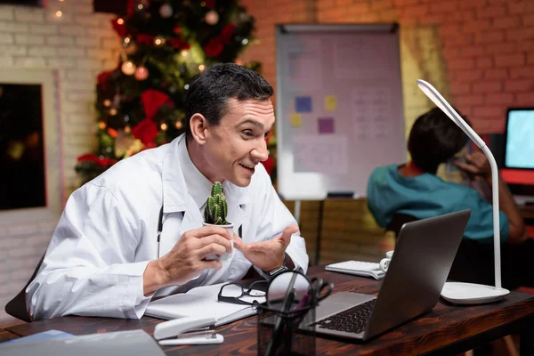 O médico trabalha na véspera de Ano Novo. Ele está a falar com alguém em vídeo. Atrás dele trabalha um colega . — Fotografia de Stock