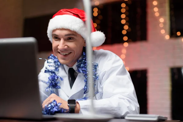 The doctor works on New Year's Eve. He put on a New Year's hat and speaks on video. — Stock Photo, Image