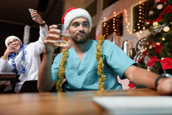 Il dottore lavora la vigilia di Capodanno. Tiene un bicchiere di whisky e guarda il monitor. . — Foto Stock