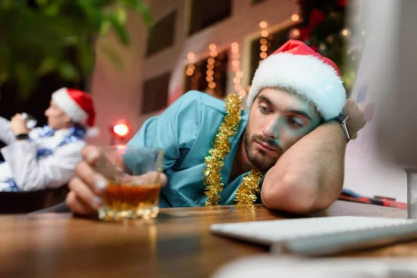 Lékař pracuje na nový rok. Boredly položí na stůl. Nedaleko je sklenku whisky. — Stock fotografie