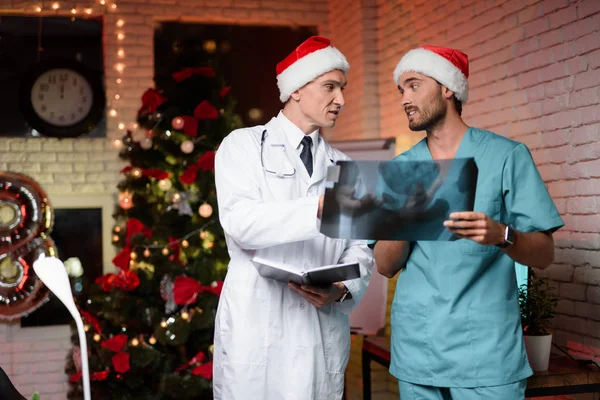 Due medici lavorano a Capodanno e discutono una radiografia che si tiene in mano . — Foto Stock