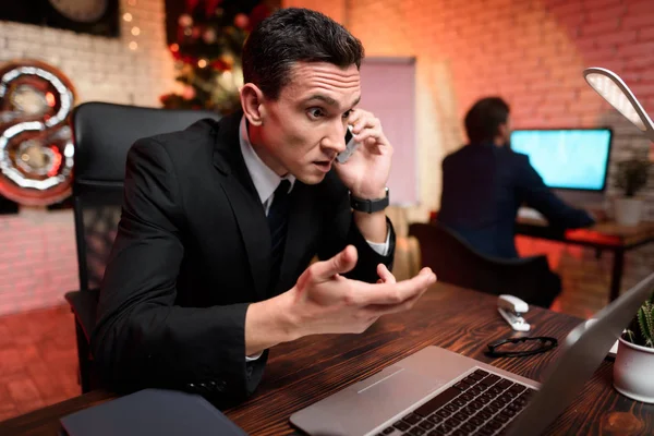 Homme d'affaires assis au bureau et travaillant la veille du Nouvel An. Il parle à quelqu'un au téléphone. . — Photo
