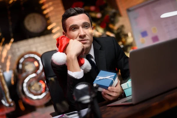 Empresario sentado en la oficina y trabajando en la víspera de Año Nuevo. Él está considerando con entusiasmo el regalo de Año Nuevo . —  Fotos de Stock