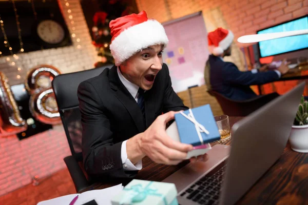 Uomo d'affari seduto in ufficio e che lavora alla vigilia di Capodanno. Sta considerando con entusiasmo il regalo di Capodanno. . — Foto Stock