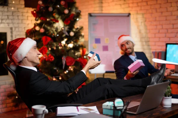 Dos hombres de negocios trabajan en Nochevieja. Se jactan de regalos el uno al otro . — Foto de Stock