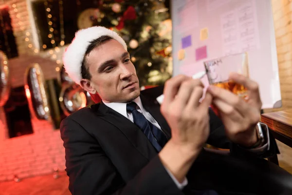 Uomo d'affari che lavora alla vigilia di Capodanno. Gli manca e scrive qualcosa con un pennarello sul bicchiere di whisky. . — Foto Stock
