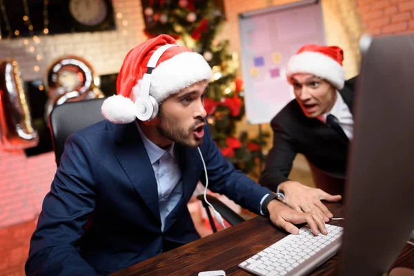 Empresario en Nochevieja en la oficina. Juega en la computadora, su colega lo observa. . —  Fotos de Stock