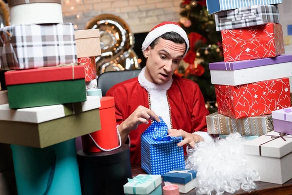 Empresário no escritório na véspera de Ano Novo. Ele usa o fato do Pai Natal. Em torno dele um monte de presentes , — Fotografia de Stock