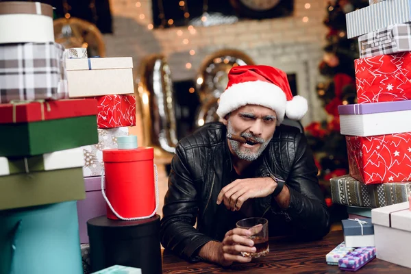 Brutal Papai Noel em uma jaqueta de couro preto senta-se com um charuto em sua boca e um copo de uísque em suas mãos — Fotografia de Stock