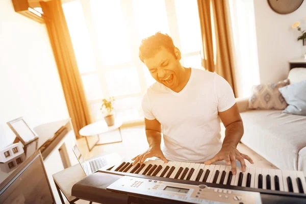 Un hombre negro se sienta en la sala de su apartamento y toca un sintetizador. Compone música. . — Foto de Stock