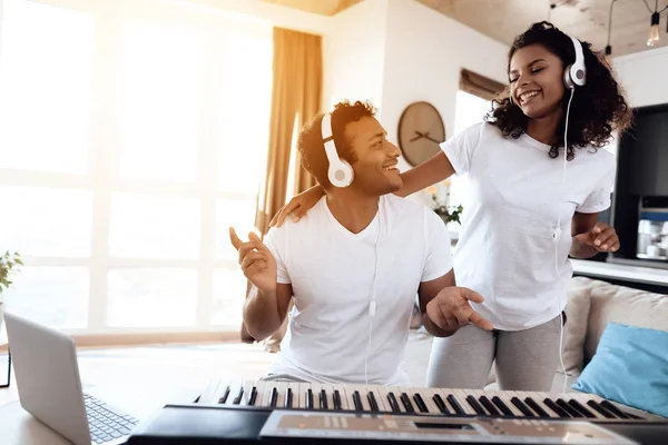 Sitzt ein schwarzer Mann im Wohnzimmer seiner Wohnung und spielt einen Synthesizer. in der Nähe seines Mädchens und er hört zu, wie er spielt — Stockfoto