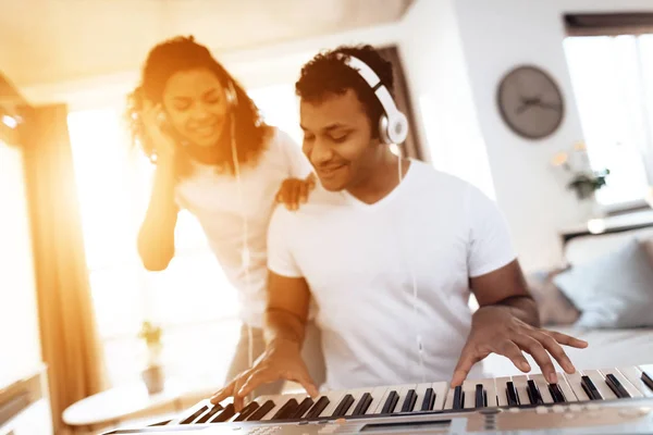 A black man sits in the living room of his apartment and plays a synthesizer. Nearby his girl and he listens as he plays — Stock Photo, Image