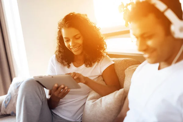 Fekete férfi és a nő ül a kanapén. Egy ember van működő-ra egy laptop, egy nő olvas valamit a tabletta. — Stock Fotó