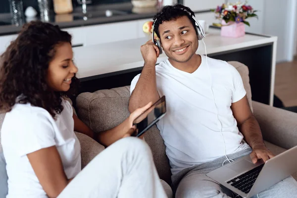 Zwarte man en vrouw zitten op de Bank. Een man is bezig met een laptop, een vrouw is het lezen van iets op een Tablet PC. — Stockfoto