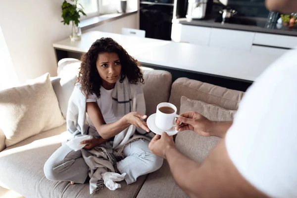 Hombres y mujeres negros están sentados en el sofá. La mujer tiene un resfriado y el hombre le trajo té caliente. . — Foto de Stock