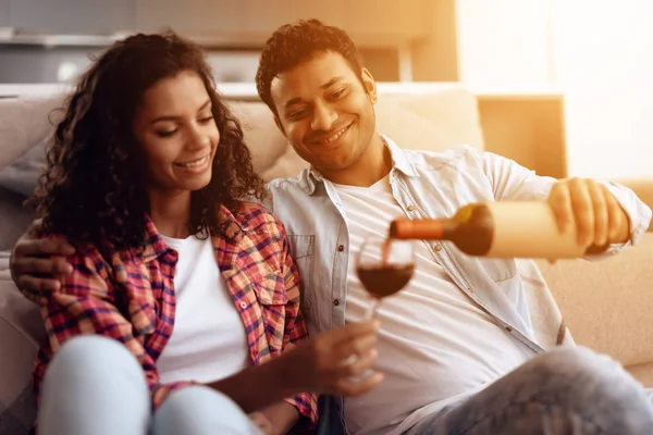 Black man and woman are sitting on the couch. A man and a woman embraced and drank wine. — Stock Photo, Image