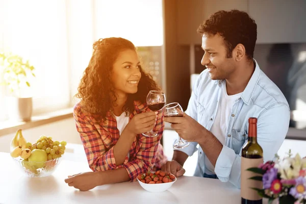 Svarta män och kvinnor i köket hemma dricker vin. De hålla glasögon i händerna och titta på varandra. — Stockfoto