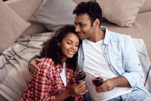 Black man and woman are sitting on the couch. A man and a woman embraced and drank wine.