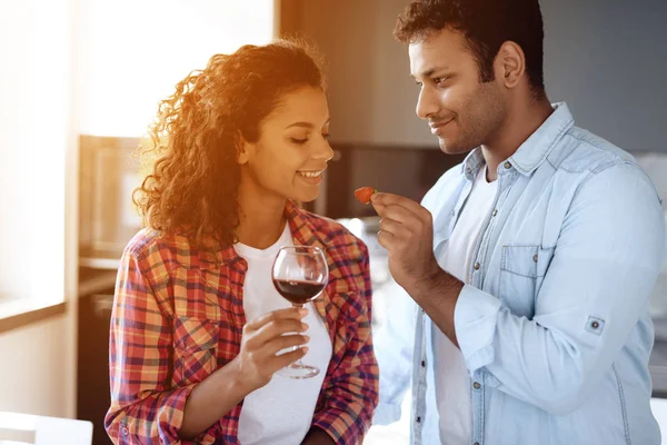 Black men and women in the kitchen at home drink wine. They look at each other with tenderness and love.