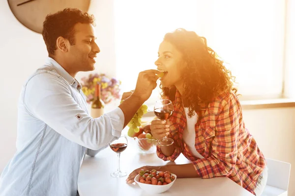 Svarta män och kvinnor i köket hemma dricker vin och äter jordgubbar. — Stockfoto