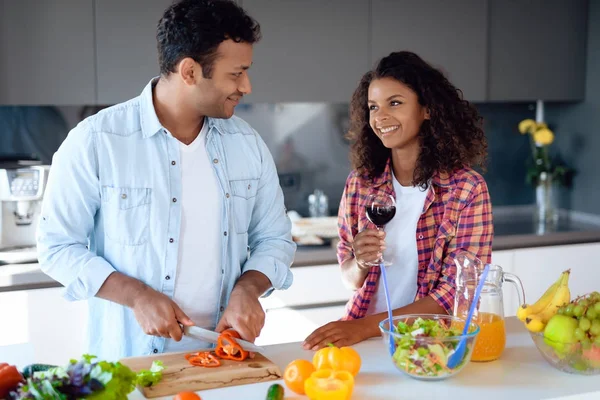 Homme et femme noirs dans la cuisine à la maison. Ils préparent le petit déjeuner, une femme se tient à proximité et boit du vin . — Photo