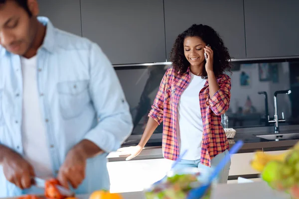 Homme et femme noirs dans la cuisine à la maison. Ils préparent le petit déjeuner, la femme parle sur le smartphone . — Photo