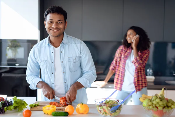 Homme et femme noirs dans la cuisine à la maison. Ils préparent le petit déjeuner, la femme parle sur le smartphone . — Photo