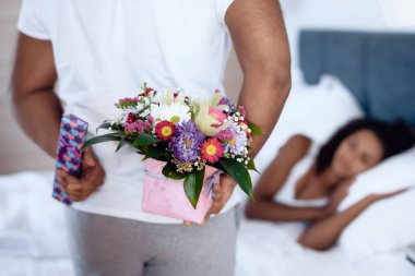 Siyah erkek ve kadın yatak odasında. Kadın yatağında yatıyor ve adam ona bir hediye hazırladı.