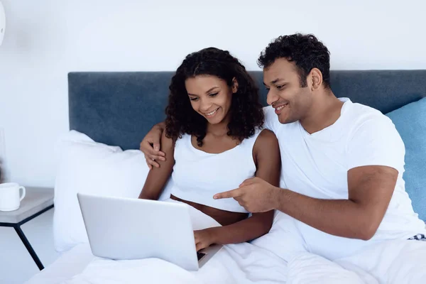Чорний чоловік і жінка в спальні. Жінка працює за ноутбуком, чоловік щось читає на планшеті . — стокове фото