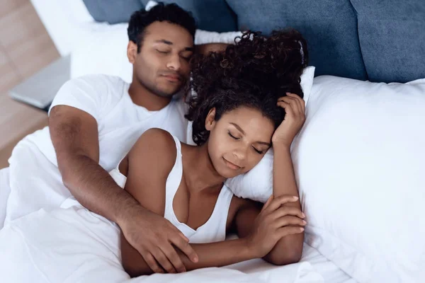 Black man and woman in the bedroom. A woman is lying in bed and her man is hugging her. They sleep embracing each other. — Stock Photo, Image