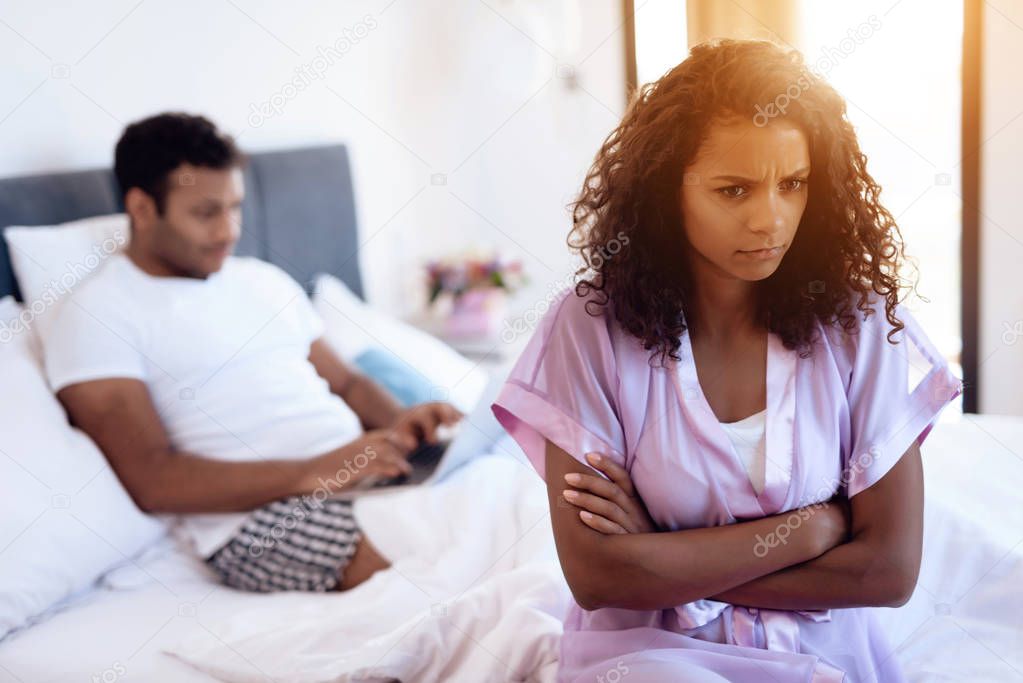 A man is lying on the bed with a laptop on his lap. Before him is his girl in sexy lingerie. The man ignores her.