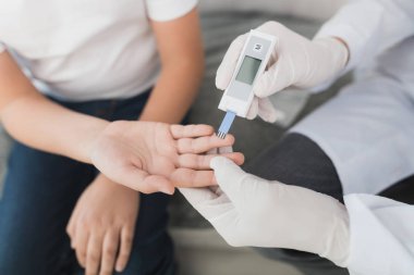 Beyaz Medikal Ürünler doktor çocuğun kan örneği şeker seviyeye taşıyor. Onlar gri kanepede oturuyor.