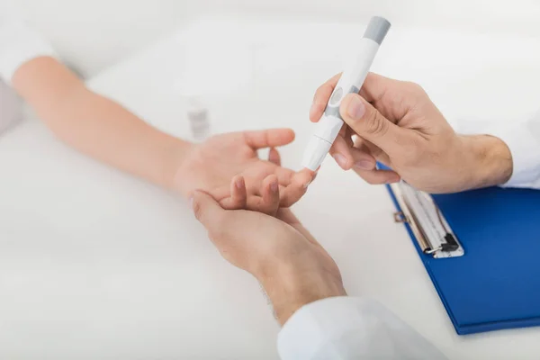 O médico tira uma amostra de sangue do rapaz para verificar se há açúcar. O menino suporta pacientemente o procedimento — Fotografia de Stock