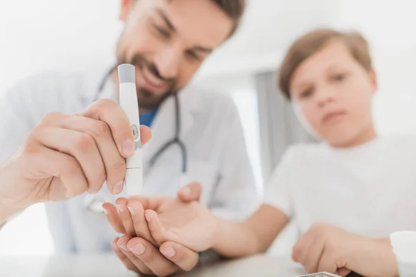 Le médecin prélève un échantillon de sang sur le garçon pour vérifier s'il n'y a pas de sucre. Le garçon supporte patiemment la procédure — Photo