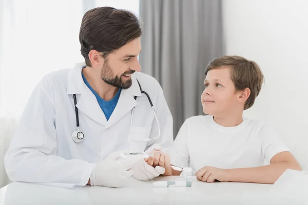 Le médecin prend le sang du garçon avec un doigt à l'aide d'un scarificateur. Le garçon supporte farouchement la procédure . — Photo