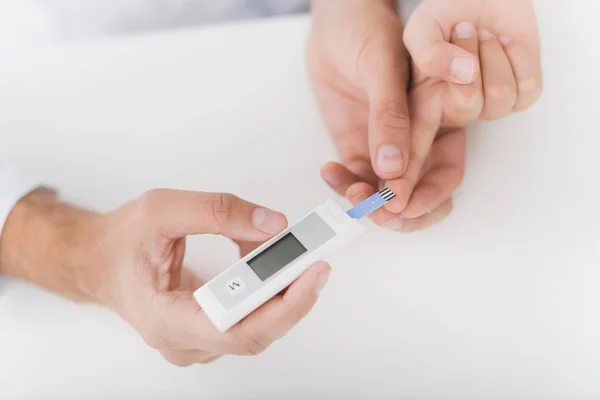 Il dottore prende il sangue dal ragazzo con un dito usando uno scarificatore. Fanno la procedura sul tavolo nello studio medico . — Foto Stock