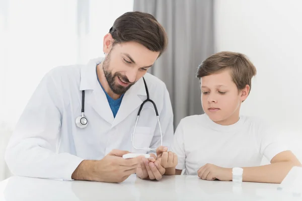 El médico toma la sangre del niño con un dedo usando un escarificador. El chico soporta firmemente el procedimiento. . — Foto de Stock